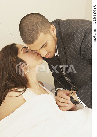 Hispanic woman in bed kissing Hispanic man in suit  11633436
