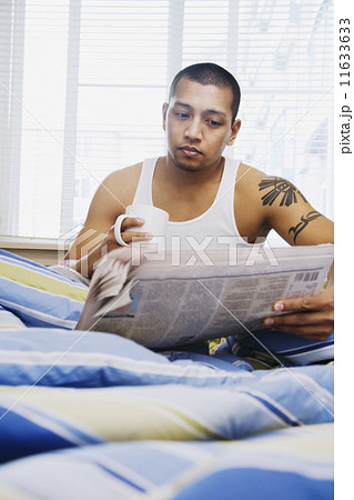 Asian man reading newspaper in bed 11633633