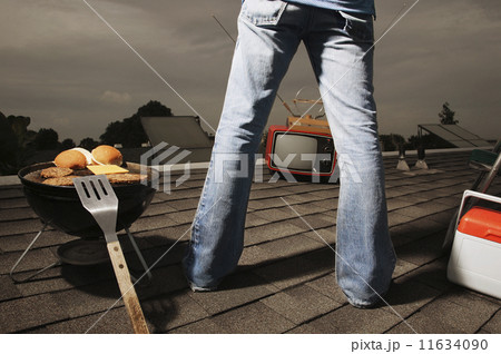 Young man watching television and barbecuing on roof Young man watching television and barbecuing on roof 11634090