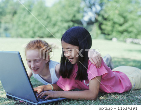 Two girls laying in park with laptop Two girls laying in park with laptop 11634391