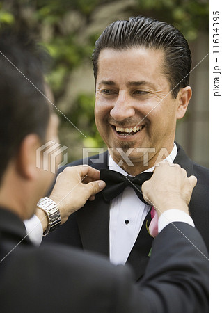 Hispanic man having bowtie adjusted 11634396
