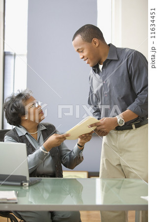 Mature woman handing man file in office Mature woman handing man file in office 11634451