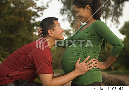 Pregnant Asian couple smiling at each other 11634644