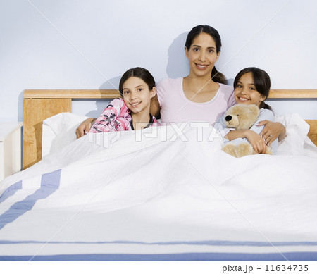 Hispanic mother and daughters sitting in bed 11634735
