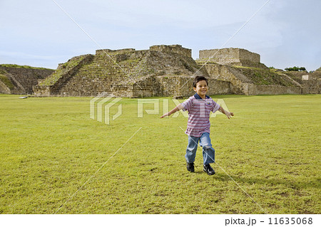 Hispanic boy running in front of ruins, Oaxaca, Mexico 11635068