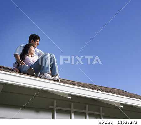 Multi-ethnic couple sitting on roof 11635273