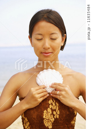 Asian woman holding seashell against chest 11635484