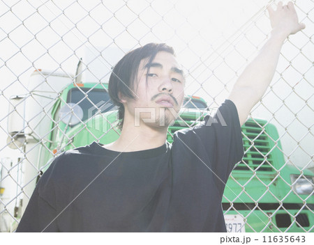 Young Asian man leaning against metal fence 11635643