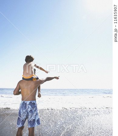 Rear view of boy sitting on father's shoulders looking at ocean Rear view of boy sitting on father's shoulders looking at ocean 11635907