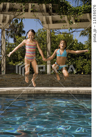 Two girls jumping into swimming pool 11636076