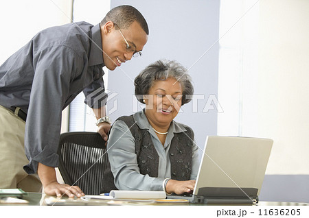 Man leaning over desk of mature woman with computer 11636205