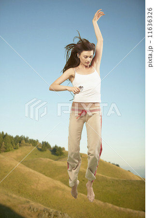 Full view of woman jumping in air while listening to music 11636326