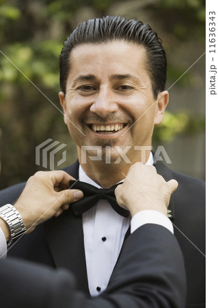 Hispanic man having bowtie adjusted 11636343