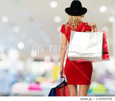 Blond woman in hat and red dress with shopping bags in shop interior 11640456