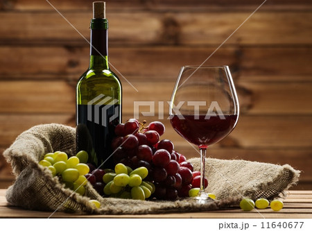 Bottle of red wine, glass and grape on a sack in wooden interior 11640677