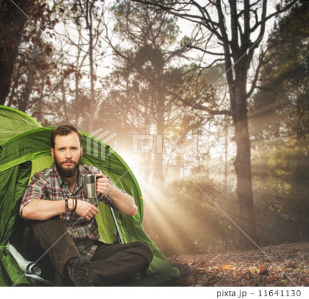 Handsome traveler near tent with coffee cup in autumnal forest 11641130