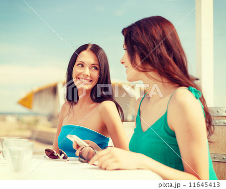 girls looking at smartphone in cafe on the beach girls looking at smartphone in cafe on the beach 11645413