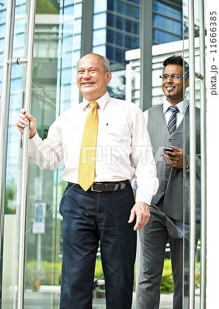 Senior businessman coming out of building with young businessman behind Senior businessman coming out of building with young businessman behind 11666385