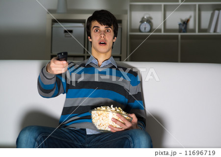 young man watching television with popcorn 11696719