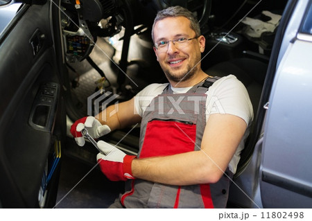 Cheerful mechanic with wrench fixing something in a car interior 11802498