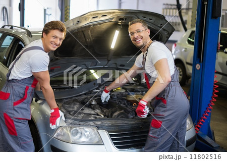 Two cheerful mechanic fixing car in a workshop Two cheerful mechanic fixing car in a workshop 11802516