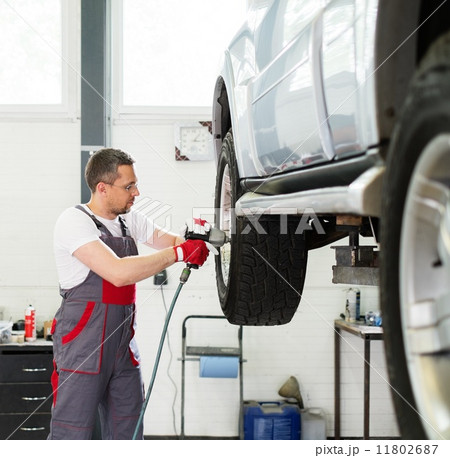 Serviceman unscrewing wheel in car workshop 11802687