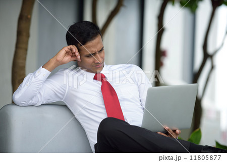 Successful young Indian corporate executive relaxing using laptop sitting down along promenade 11805877