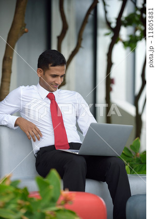 Successful young Indian corporate executive relaxing using laptop sitting down along promenade Successful young Indian corporate executive relaxing using laptop sitting down along promenade 11805881