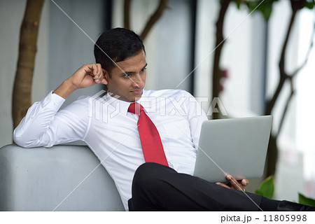 Successful young Indian corporate executive shocked while using laptop sitting down along promenade Successful young Indian corporate executive shocked while using laptop sitting down along promenade 11805998