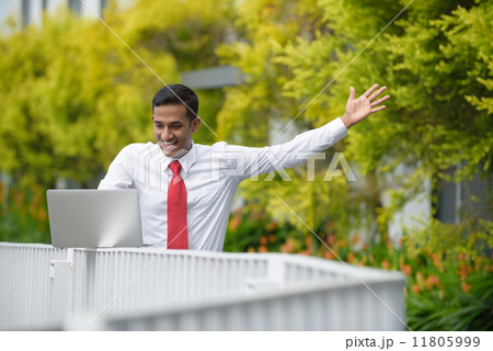 Successful young Indian corporate executive rejoicing while using laptop along promenade Successful young Indian corporate executive rejoicing while using laptop along promenade 11805999