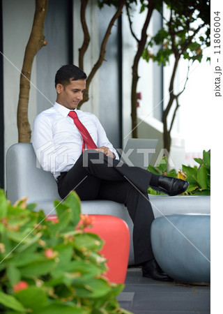 Successful young Indian corporate executive relaxing using laptop sitting down along promenade Successful young Indian corporate executive relaxing using laptop sitting down along promenade 11806004