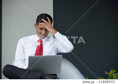 Successful young Indian corporate executive shocked using laptop sitting down along promenade Successful young Indian corporate executive shocked using laptop sitting down along promenade 11806055