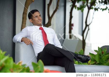 Successful young Indian corporate executive relaxing using laptop sitting down along promenade Successful young Indian corporate executive relaxing using laptop sitting down along promenade 11806171