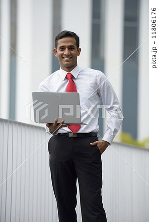 Successful young Indian corporate executive using laptop in front of concrete building Successful young Indian corporate executive using laptop in front of concrete building 11806176