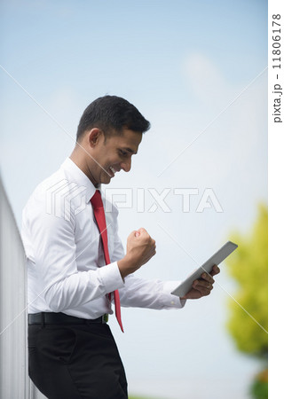 Successful young Indian corporate executive victory using iPad mobile device tablet along promenade 11806178