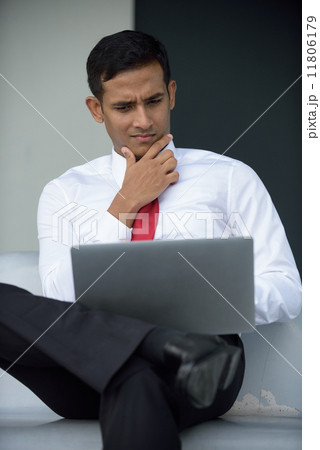 Successful young Indian corporate executive using laptop sitting down along promenade Successful young Indian corporate executive using laptop sitting down along promenade 11806179