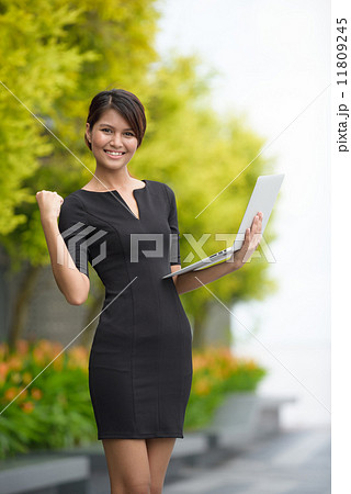 Victorious successful young Malay business woman using laptop along promenade 11809245