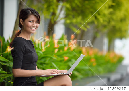 Successful young Malay business woman using laptop along promenade during break time 11809247