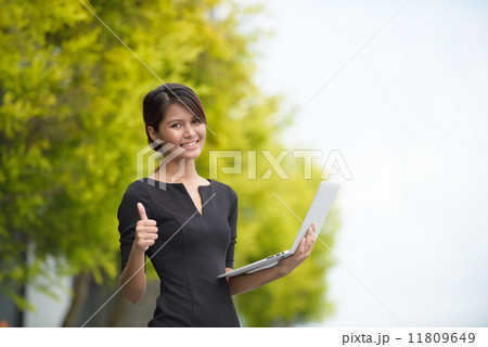 Victorious successful young Malay business woman using laptop along promenade 11809649