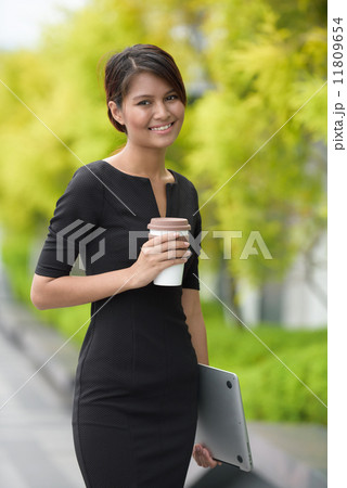 Successful young Malay business woman with coffee cup and laptop along promenade during break time Successful young Malay business woman with coffee cup and laptop along promenade during break time 11809654