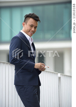 Successful young chinese businessman using smart phone in front of glass building 11810168