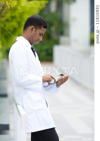 Young successful Indian medical doctor using mobile device tablet iPad along promenade Young successful Indian medical doctor using mobile device tablet iPad along promenade 11810891