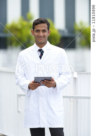 Young successful Indian medical doctor using mobile device tablet iPad along promenade Young successful Indian medical doctor using mobile device tablet iPad along promenade 11810896