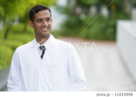 Friendly young successful Indian medical doctor along promenade 11810998