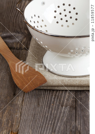 Enamel colander and a Cooking spoon stands on the kitchen table 11859577
