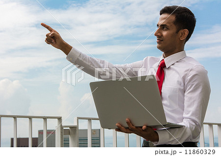 Asian businessman holding laptop, pointing up. 11860329