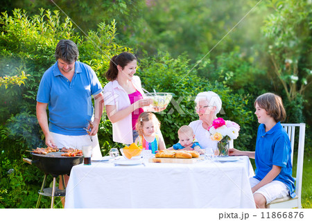 Happy big family enjoying BBQ lunch with grandmother eating grilled meat in the garden Happy big family enjoying BBQ lunch with grandmother eating grilled meat in the garden 11866876