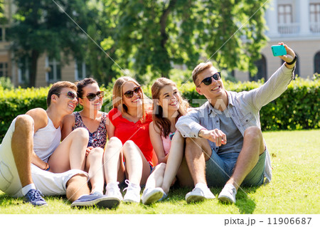 smiling friends with smartphone sitting on grass 11906687