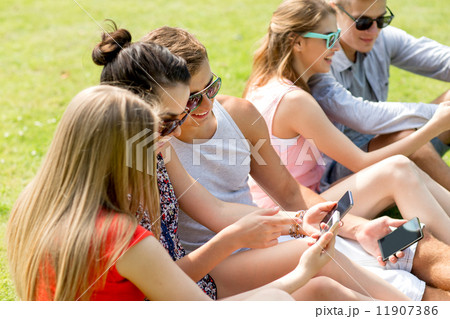 smiling friends with smartphones sitting on grass smiling friends with smartphones sitting on grass 11907386