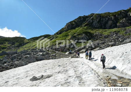 晩夏でも残る雪渓を行く登山者 11908078
